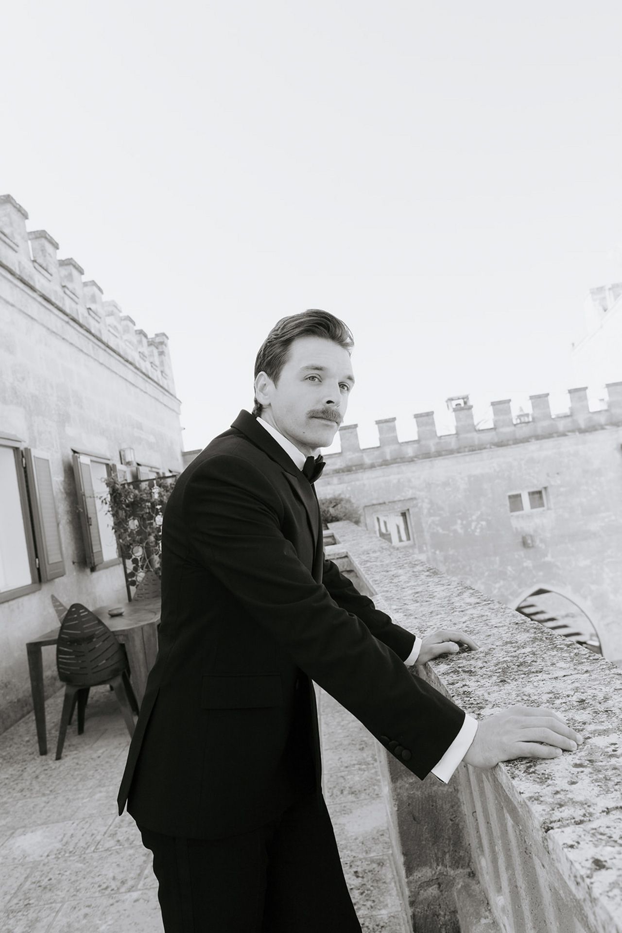A person in a black coat poses against a stone wall in a series of vintage-style black and white photographs.