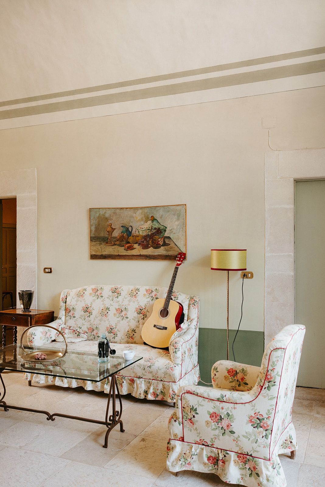 Vintage living room interior with floral upholstered chairs, acoustic guitar, and decorative painting on cream walls.