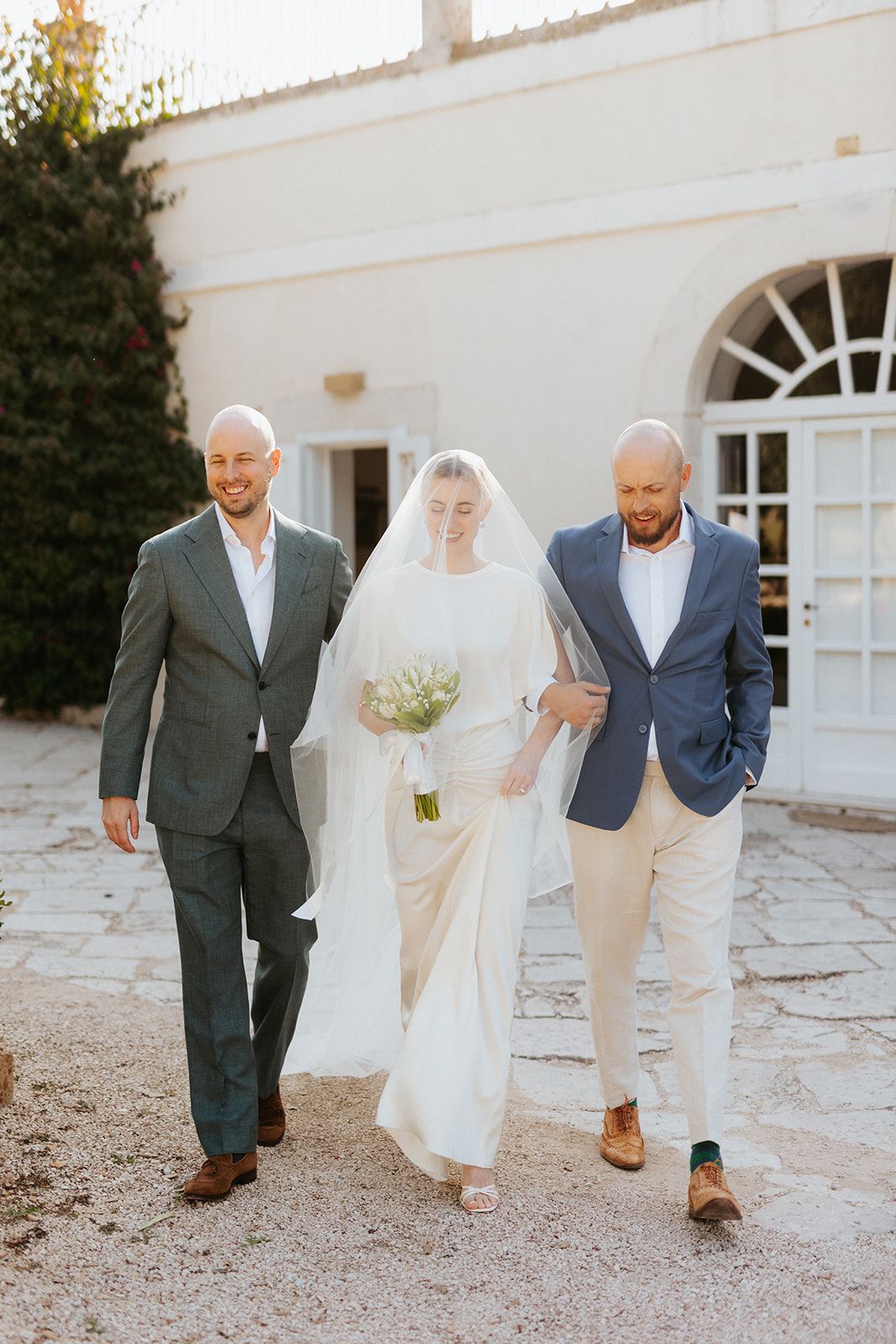A classic wedding moment captured in front of a white building with arched doorways at sunset.