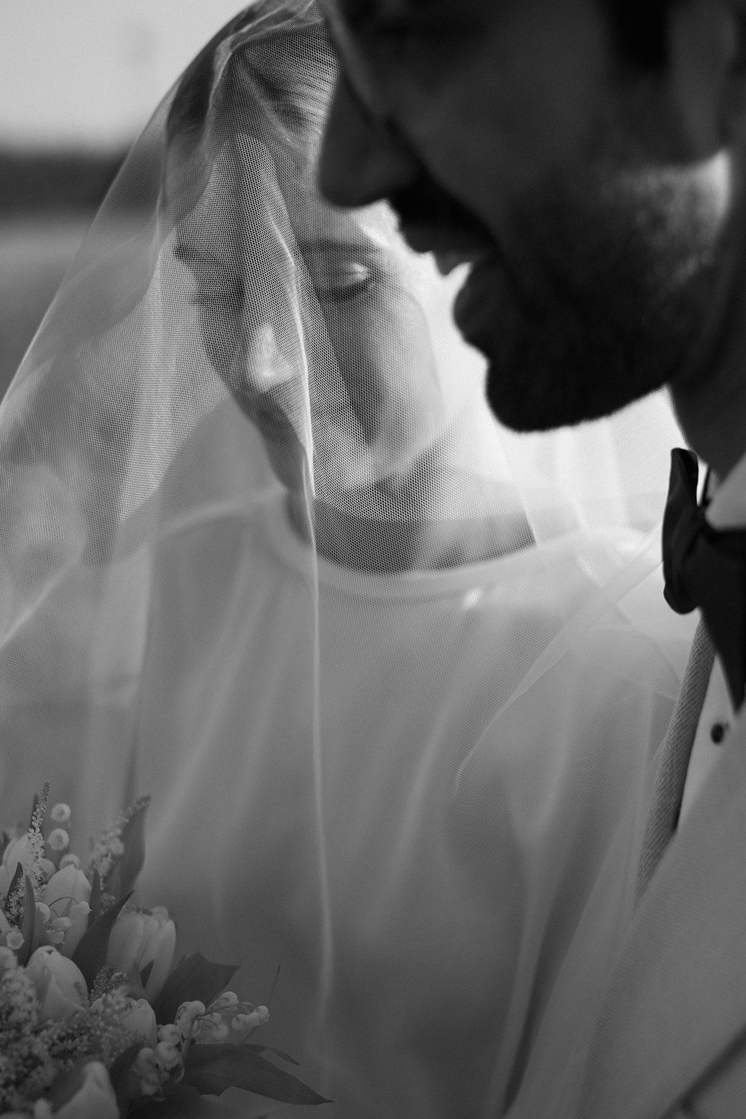 A romantic black and white wedding moment showing a couple in close embrace under a delicate veil.
