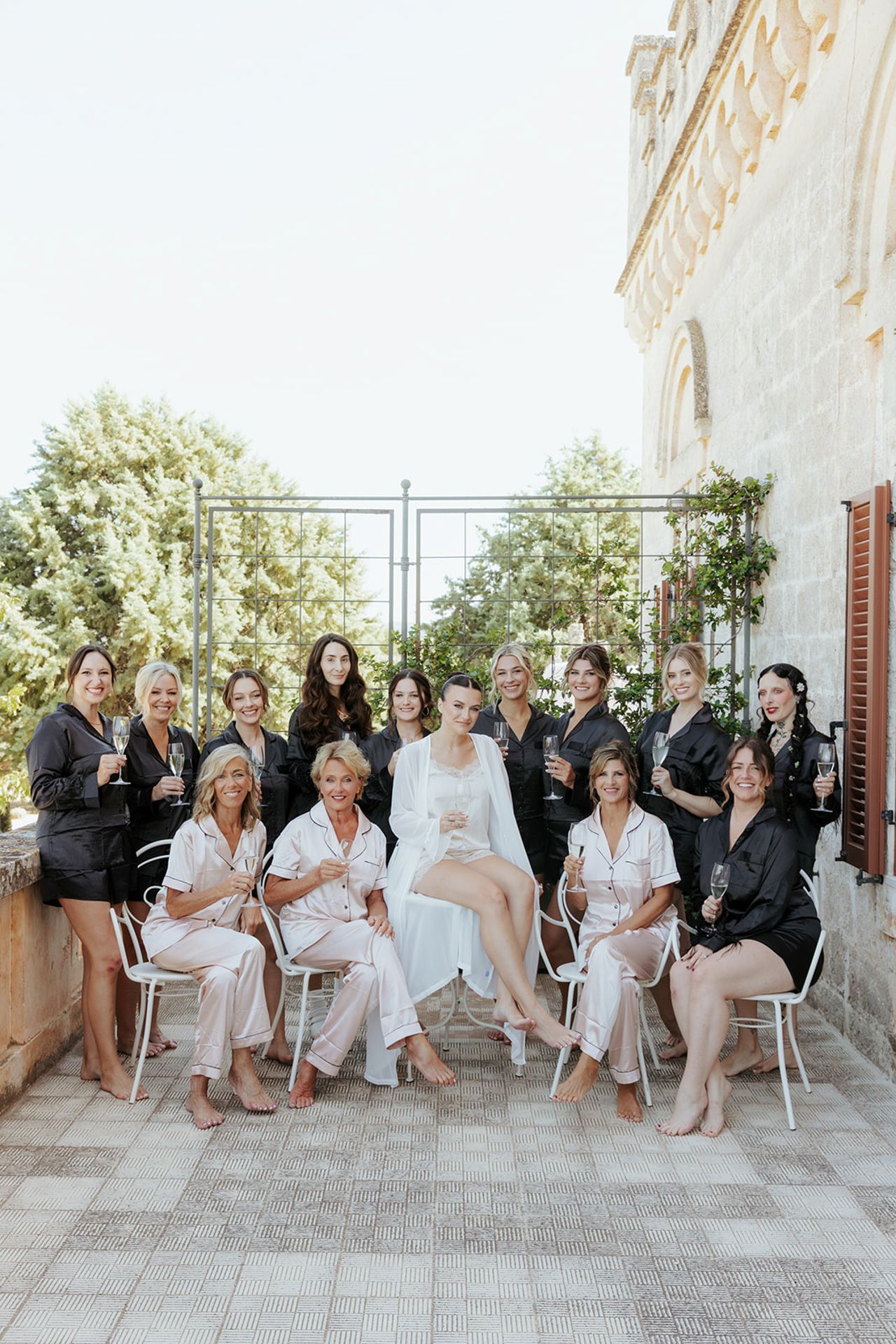 Wedding party in matching robes gather on an elegant outdoor terrace for pre-ceremony photos.