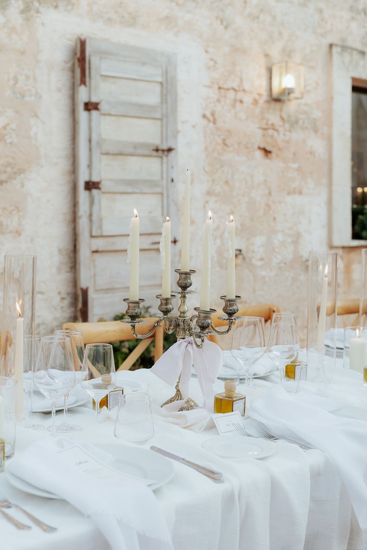 Elegant white table setting with candelabra and vintage decor against rustic stone wall.