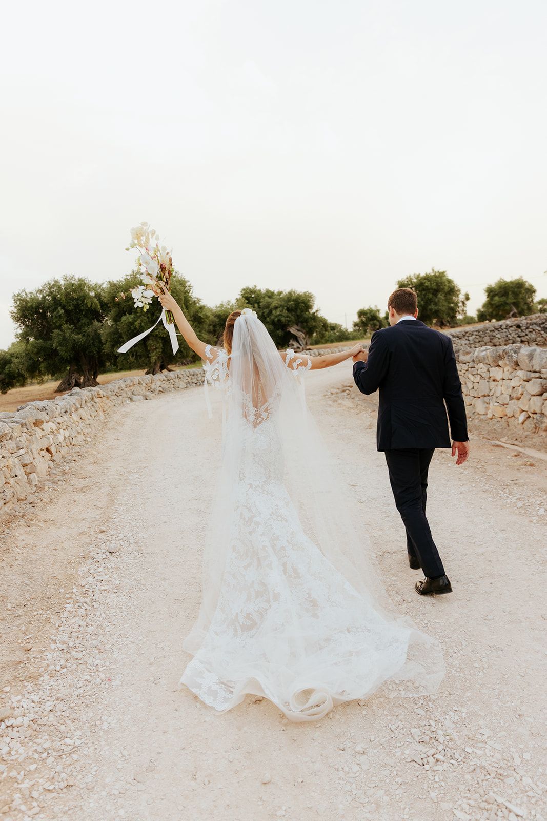 Bride and groom dancing playfully on gravel path with flowing white dress movement.