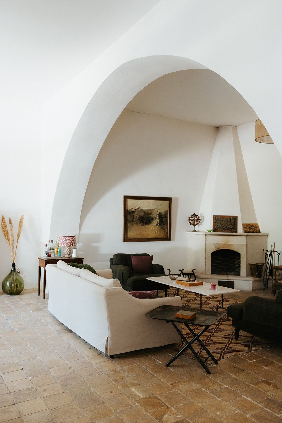 Modern rustic living room with arched doorway, white sofa, dark chairs, and natural stone flooring.