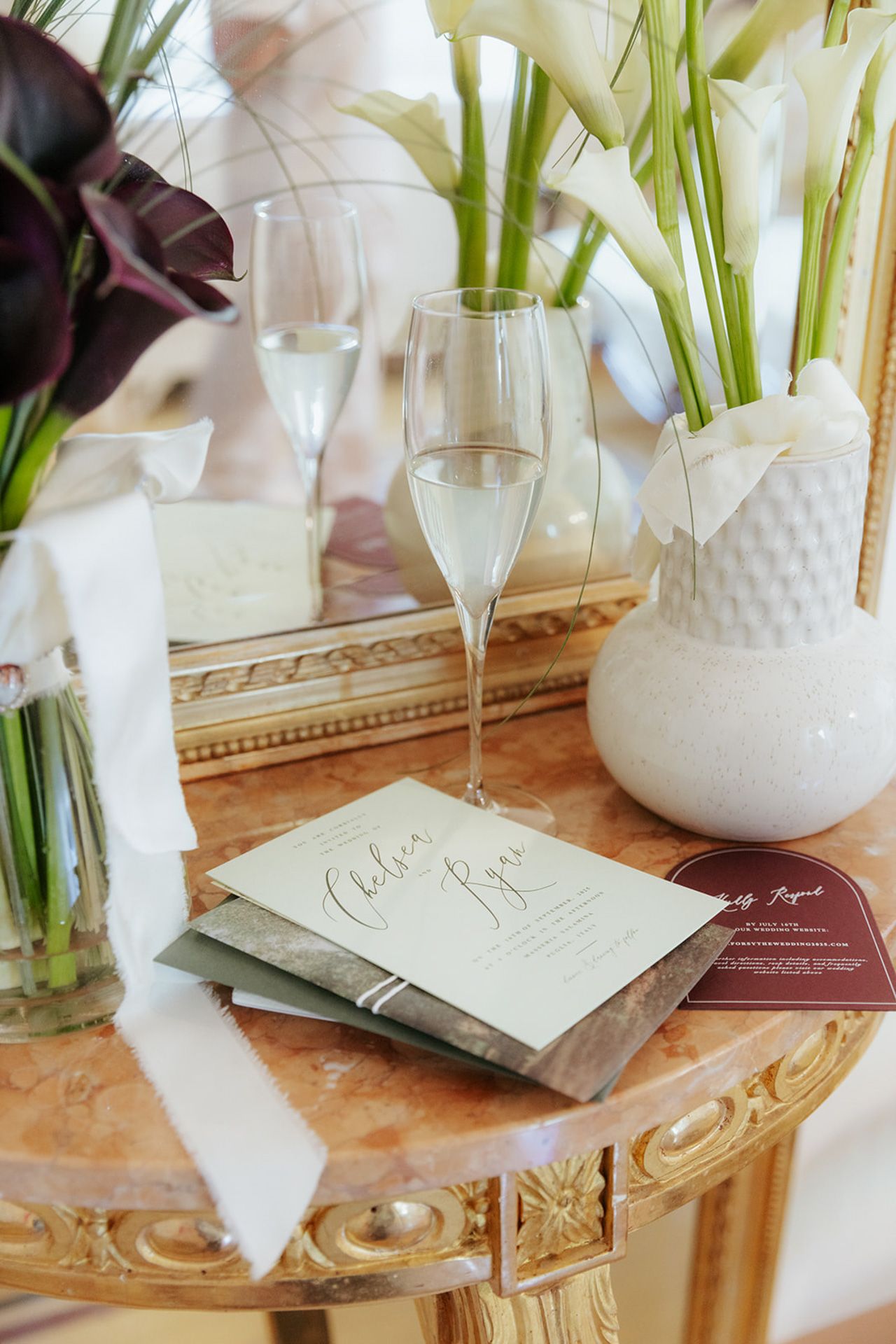 Wedding stationery and floral arrangements displayed on an ornate gold table with white vases and champagne glasses.
