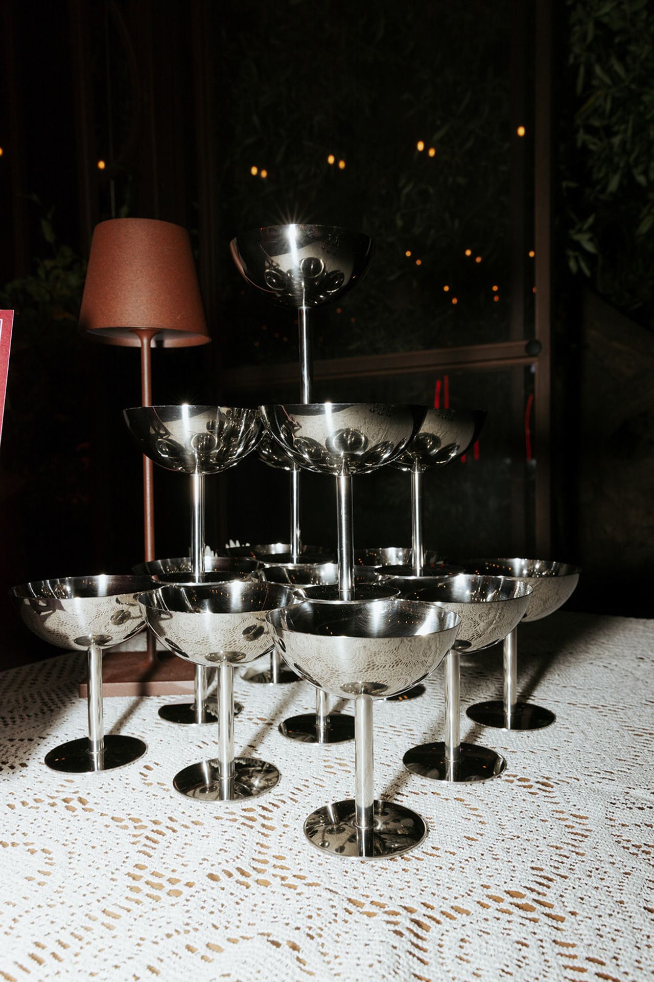 A sequence of four photos showing glowing martini glasses arranged on a white lace tablecloth at night.