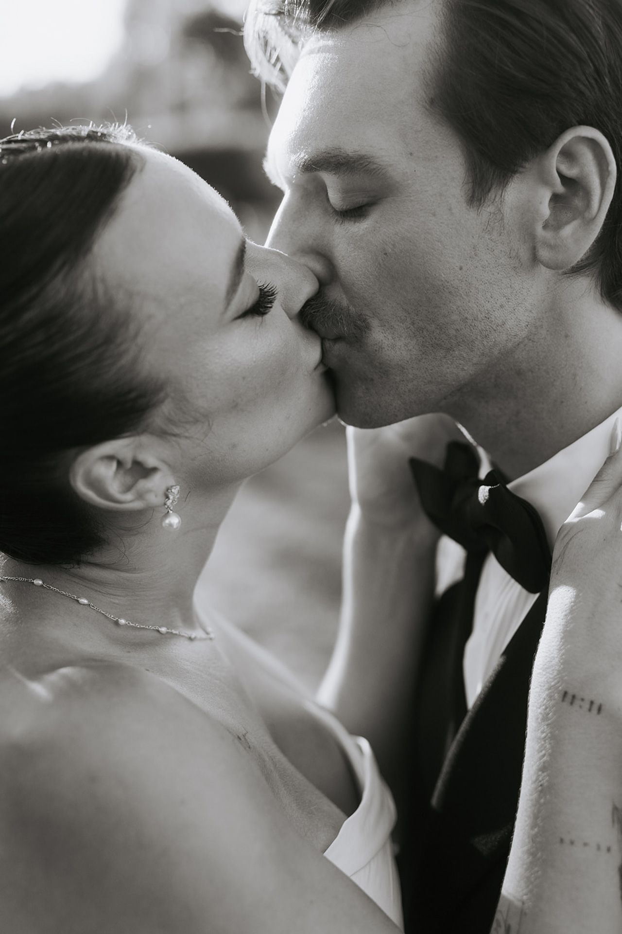 A romantic black and white photo series showing tender kisses between a bride and groom on their wedding day.