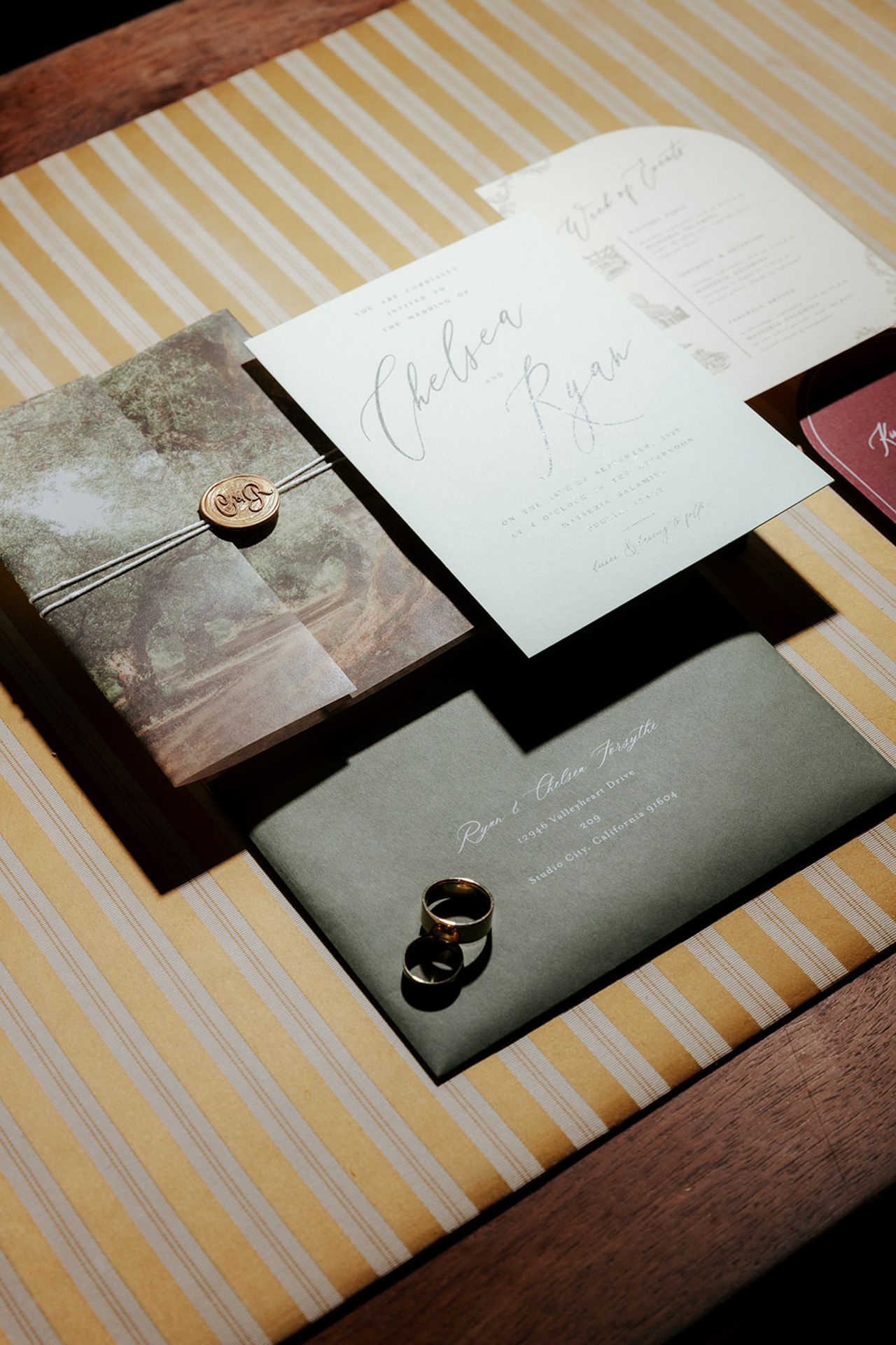 Wedding invitation suite with black and white cards displayed on a striped surface with wedding rings.