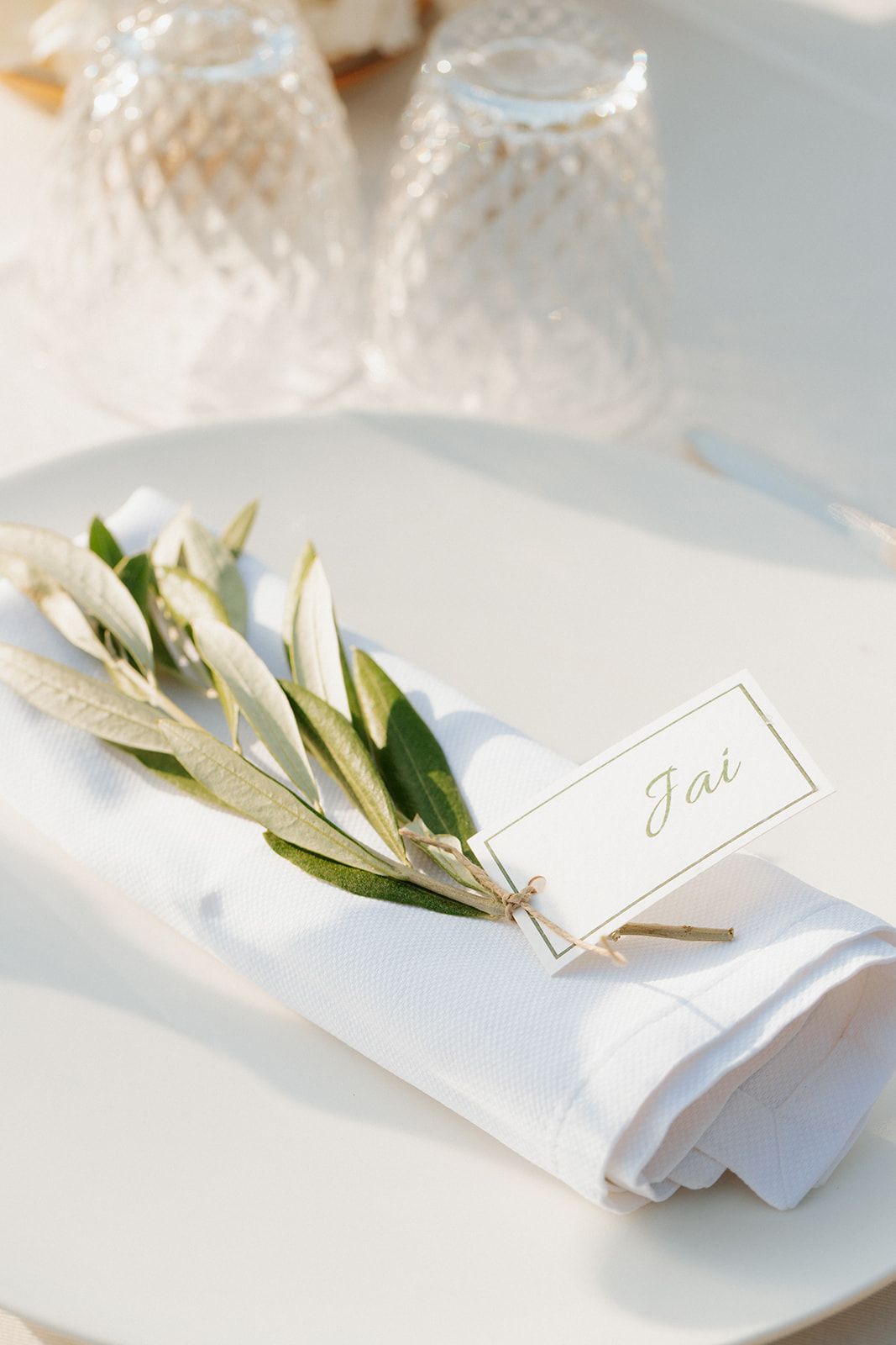 White napkin place settings with delicate olive branch decorations and name cards create an elegant table arrangement.