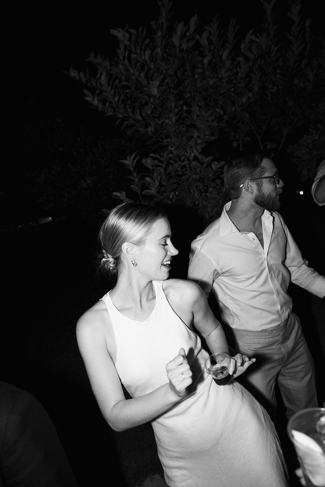 People dancing energetically at a dimly lit nighttime event in white attire.