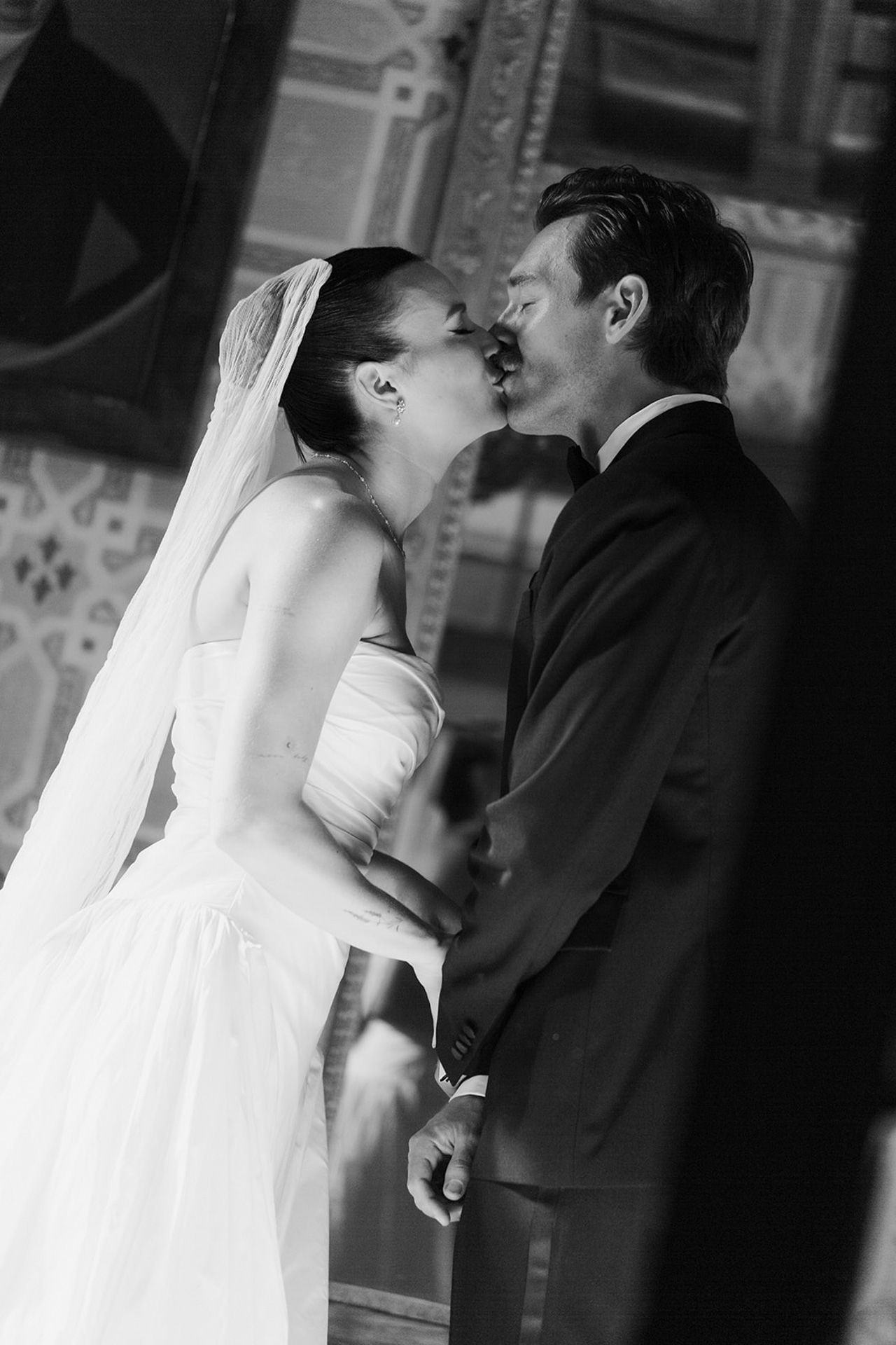 A romantic black and white wedding photo captures a tender kiss between newlyweds in formal attire.