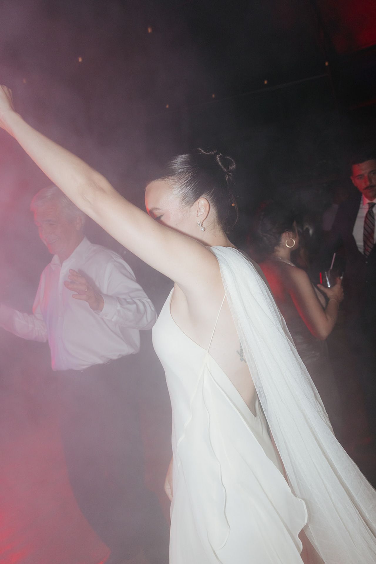 People dancing and moving in a dimly lit nightclub with red lighting and a smoky atmosphere.
