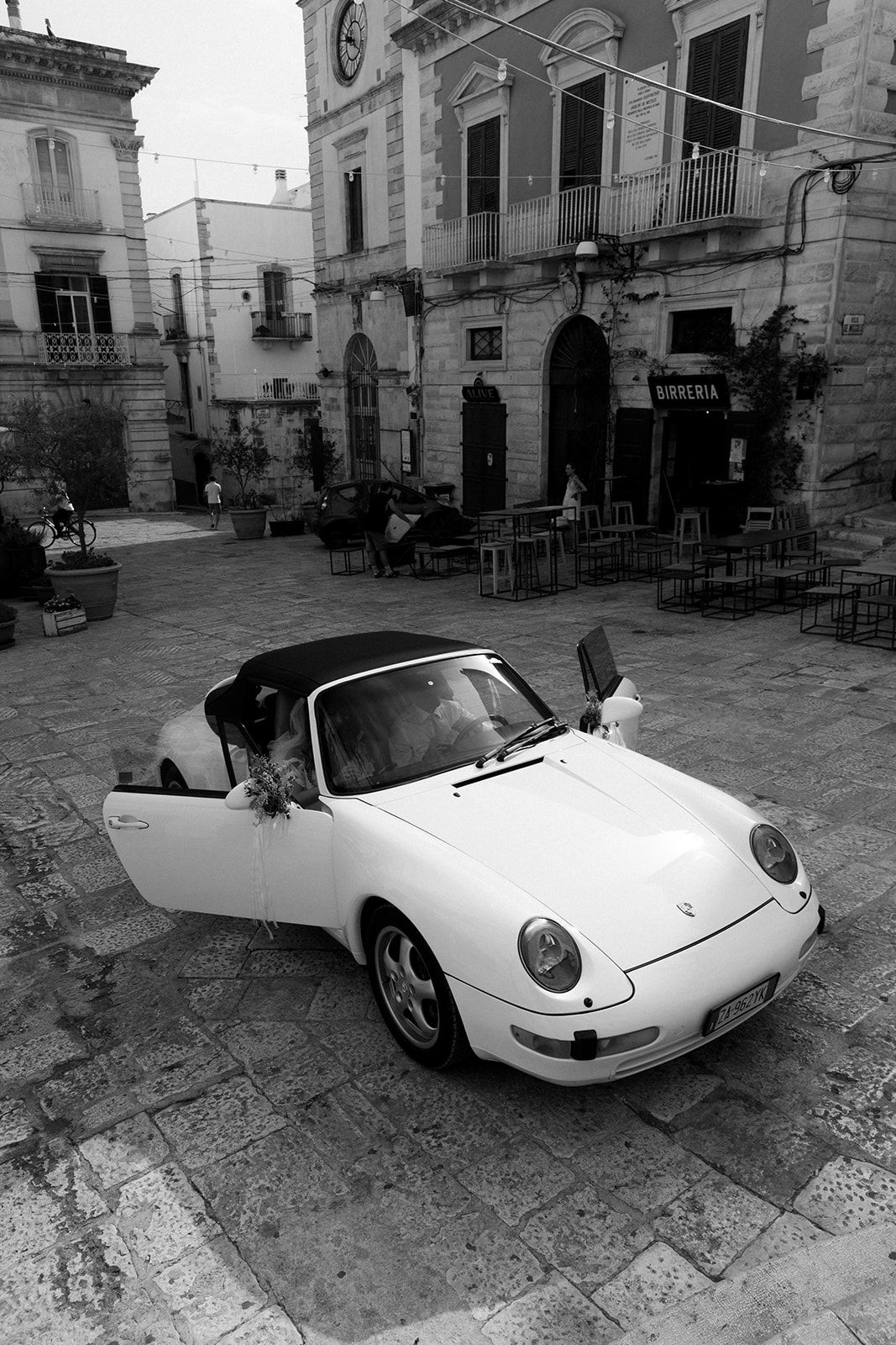 A classic white Porsche 911 convertible photographed from multiple angles in a historic European plaza setting.