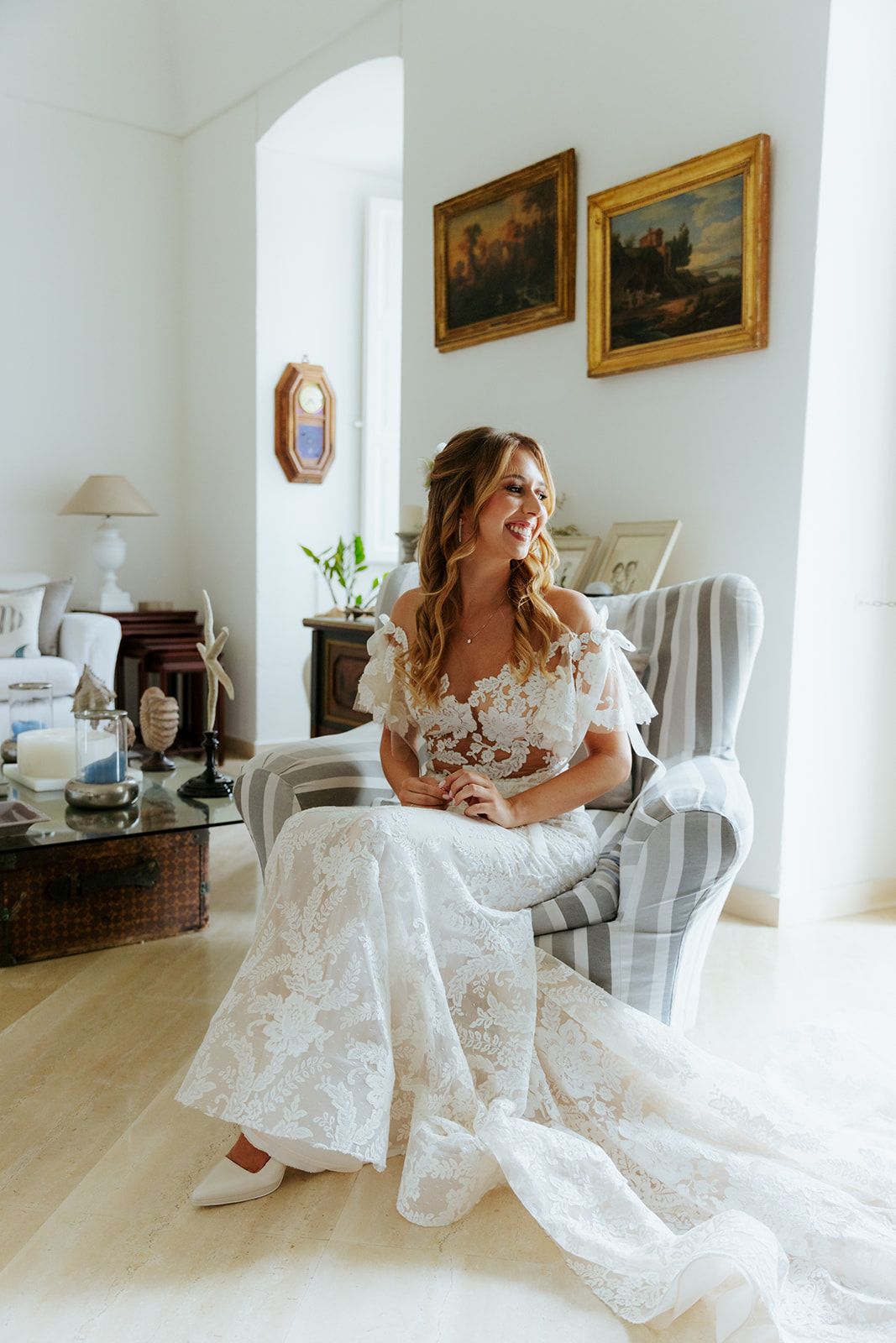 Bride in lace wedding dress twirling and dancing joyfully in an elegant white room with golden-framed artwork.