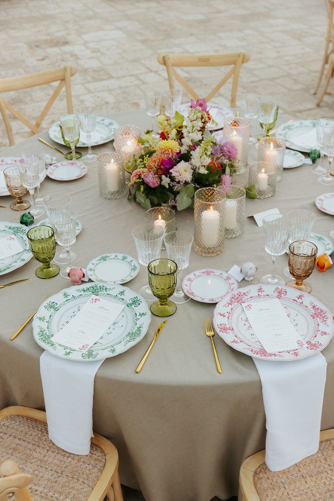 Elegant table settings with floral china plates, candles, and fresh flower centerpieces on taupe linen tablecloths.