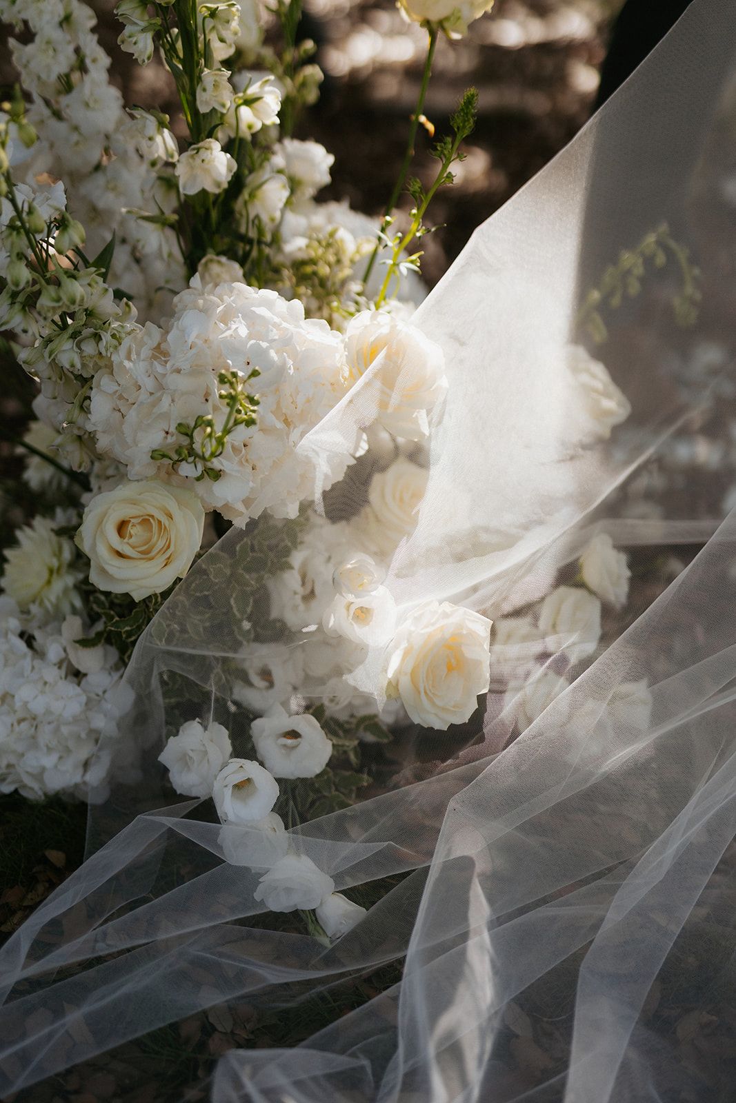 Beautiful white roses and delicate tulle veil create an ethereal bridal arrangement in soft natural light.