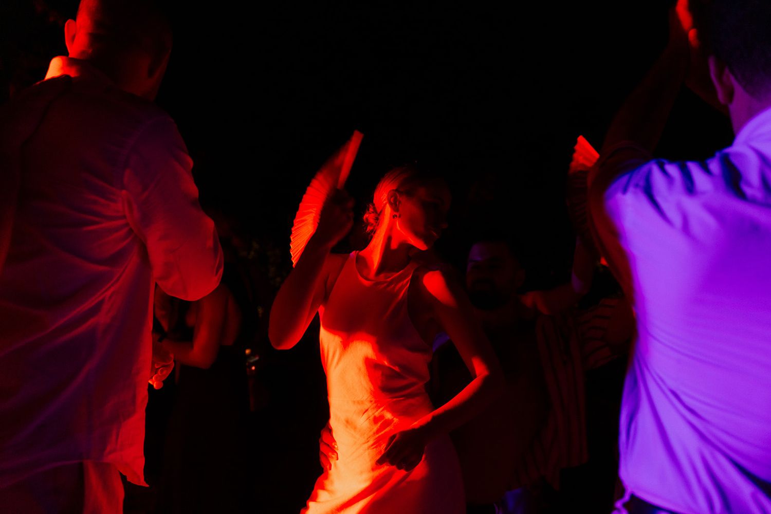People dance and celebrate at a nightclub with vibrant red and purple lighting effects creating an energetic atmosphere.