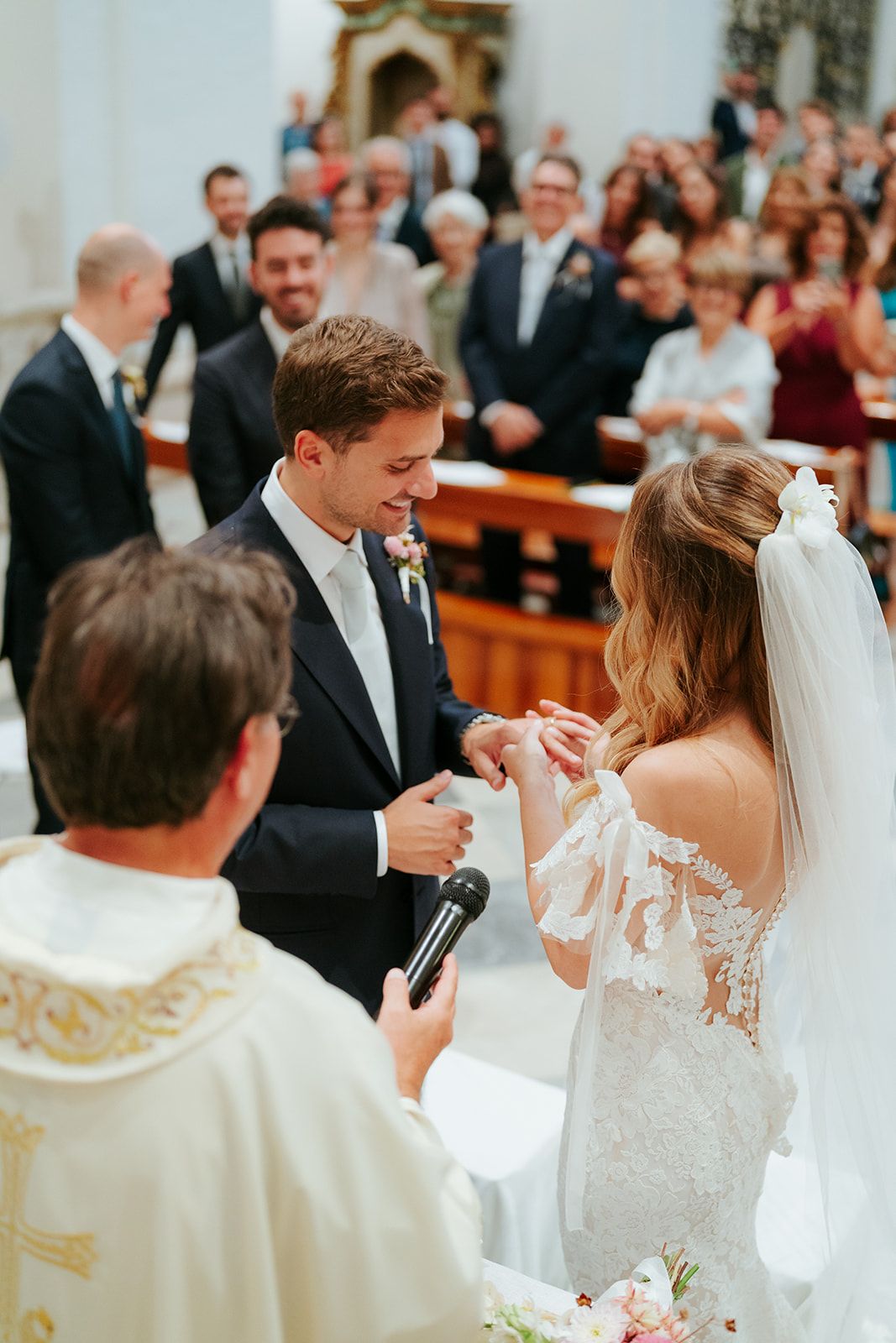 A couple and wedding guests perform unity ceremony rituals during traditional Catholic church ceremony.