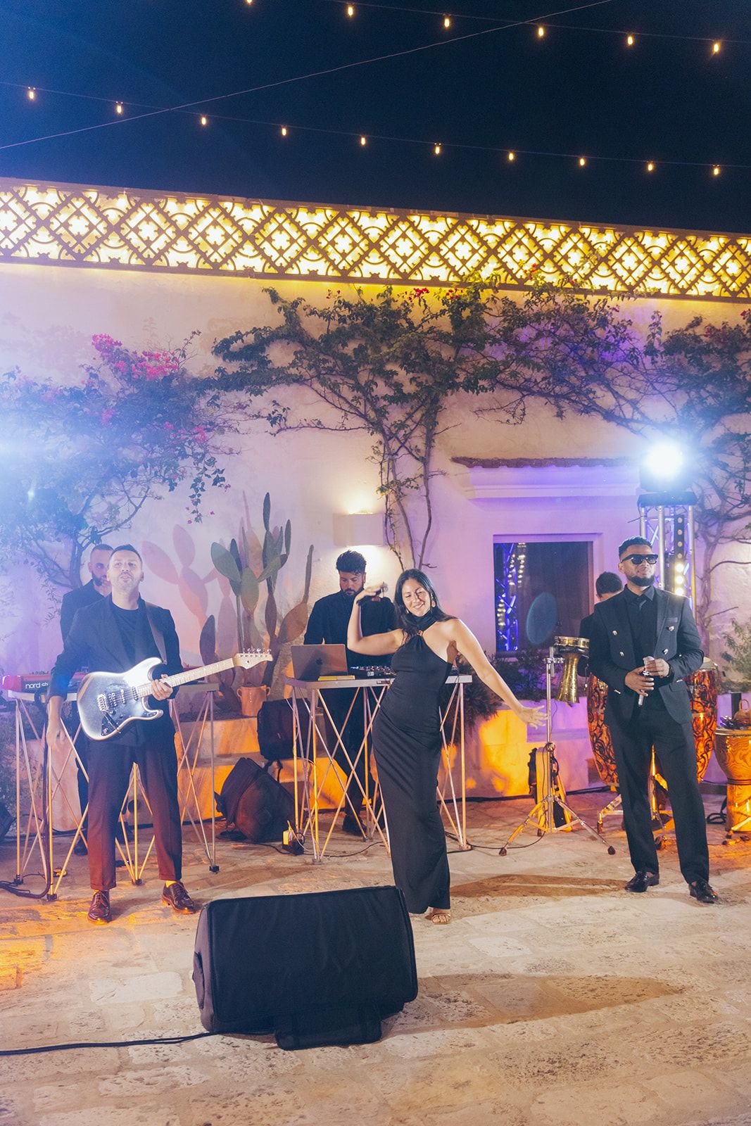 Musicians perform outdoors at night under string lights and rustic decor creating an intimate ambiance.