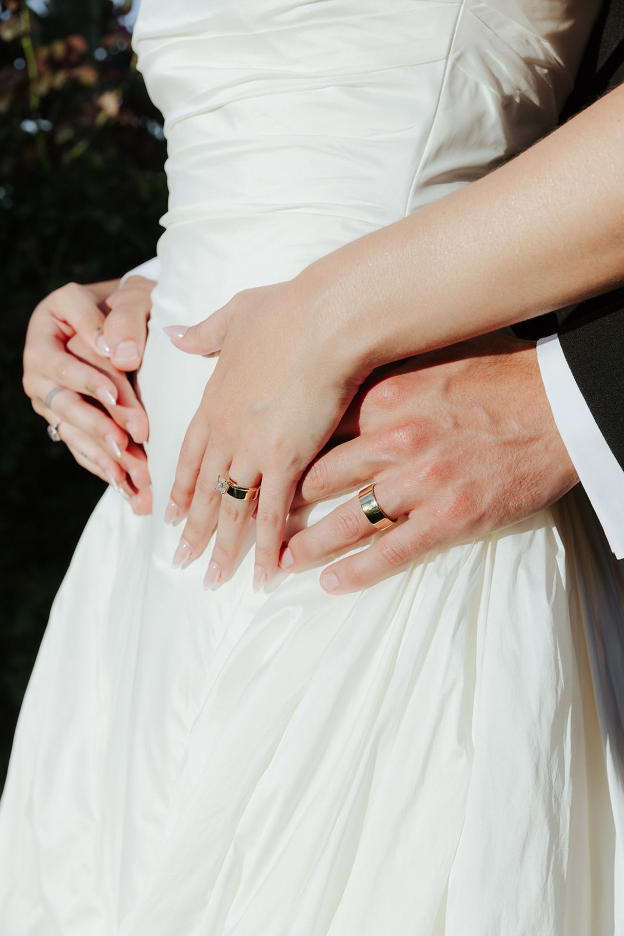 Close-up of wedding rings and hands on a white wedding dress showing both bride and groom's bands.