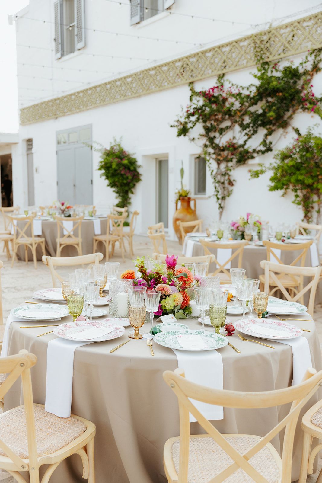 Elegant outdoor wedding reception setup with white tablecloths, light wooden chairs and floral centerpieces.
