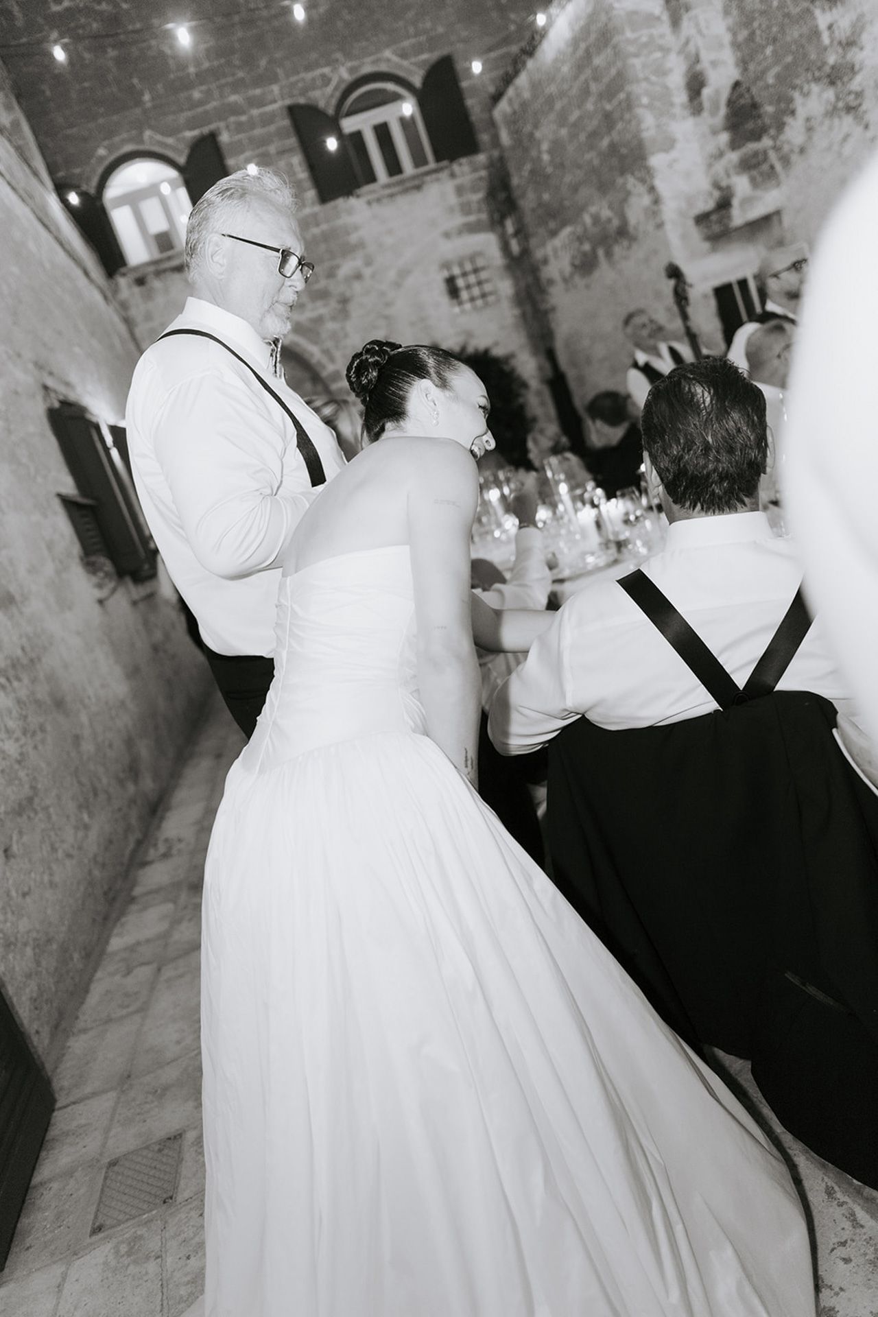 A couple in wedding attire dances together during their first dance at a rustic indoor reception venue.