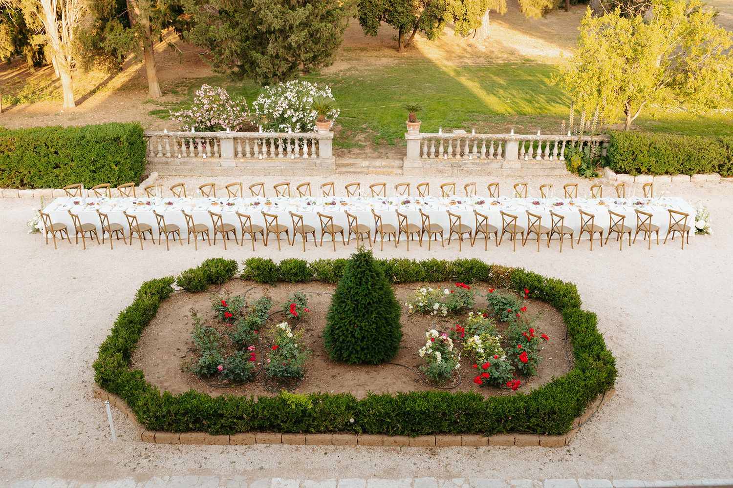 Aerial view of elegant outdoor wedding ceremony setup with rows of chairs facing a landscaped flower garden.