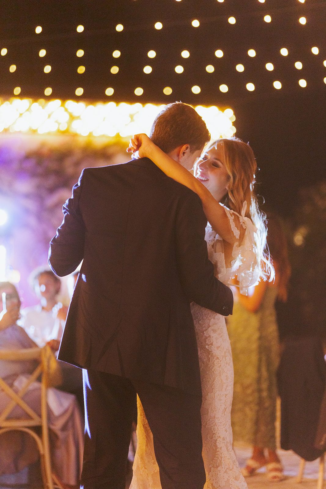 A romantic first dance at a wedding reception glows under soft lighting as the couple embraces and moves together.