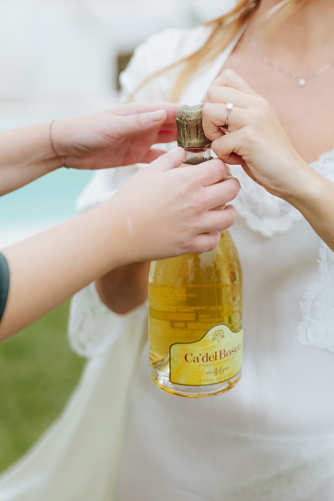 Hands holding and opening a bottle of Ca Del Bosco champagne with a light green background.
