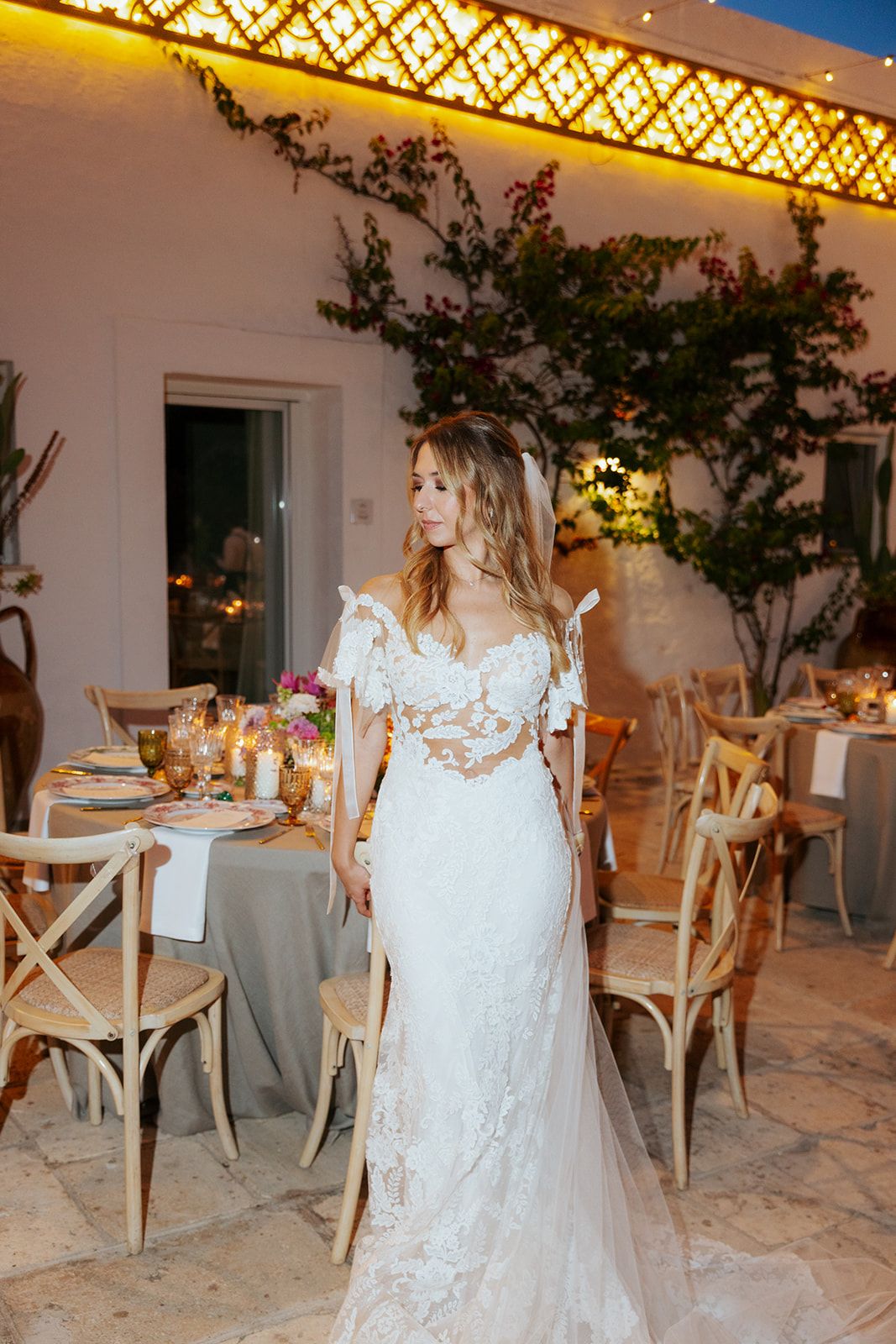 A stunning wedding reception venue with white decor, rustic wooden chairs and overhead lighting creates an elegant atmosphere.