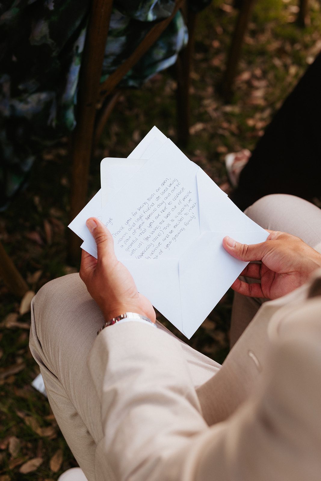 A person in beige clothing reads a handwritten letter while sitting outdoors among fallen leaves.