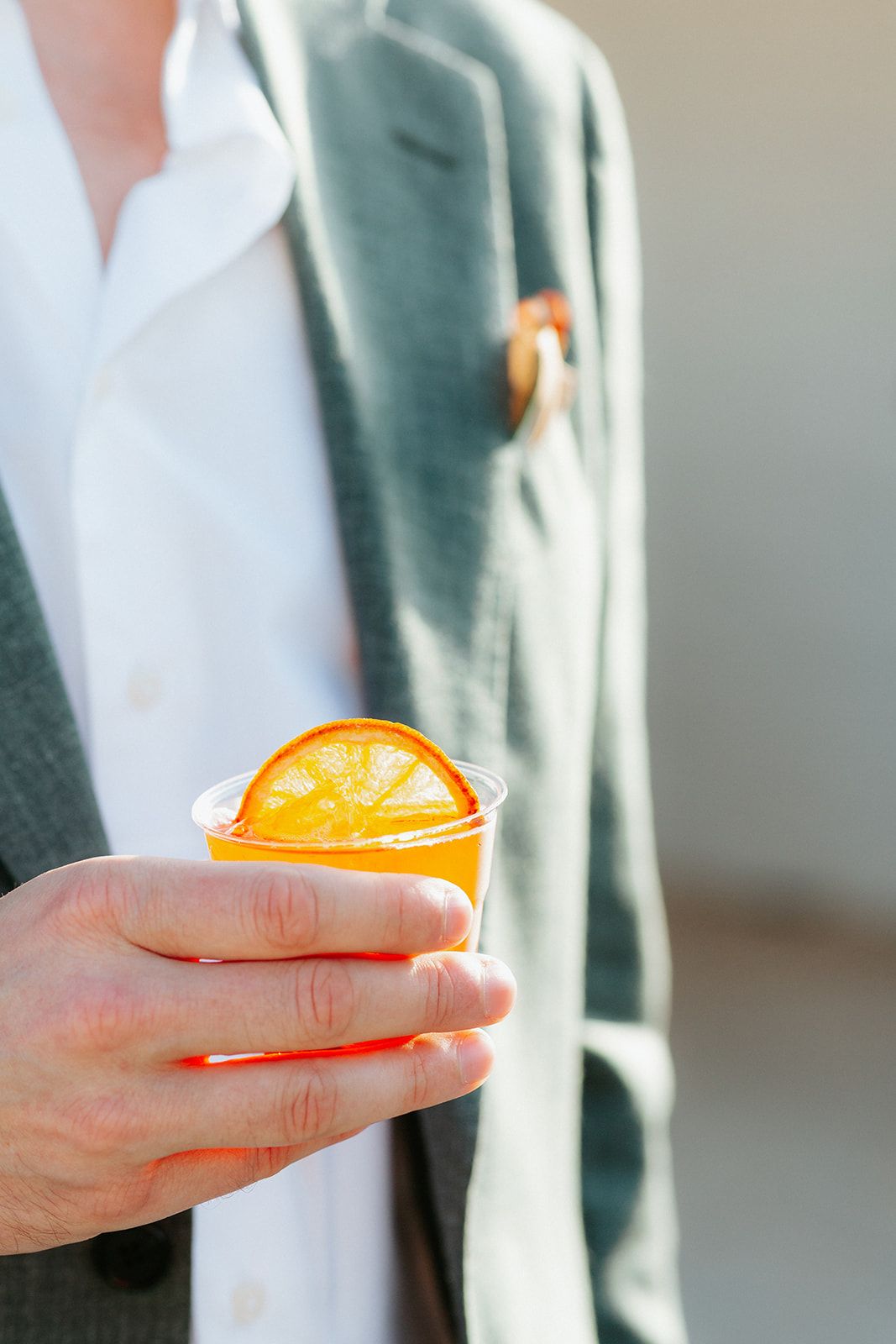 Hand holding and displaying sliced orange against blurred green and white background.