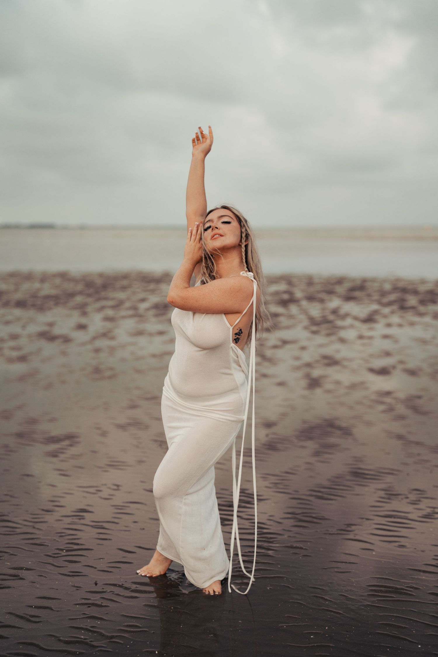 Artistic beach portraits with person in white dress posing dramatically on wet sand. Earlhams Beach, Harwich, Essex.