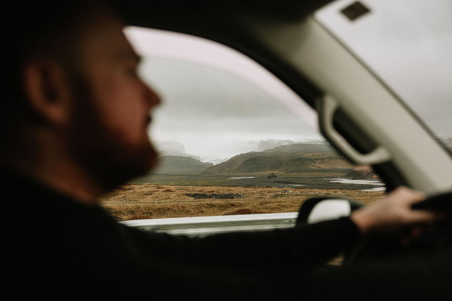 View through a car windshield of a winding mountain road during an overcast day. Icleand.