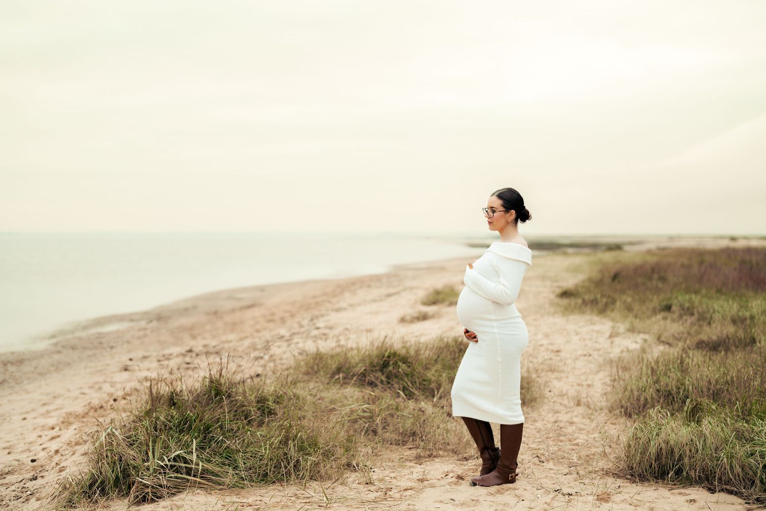 Person in white sweater walking along coastal path with grassy dunes. Earlhams Beach, Harwich, Essex.