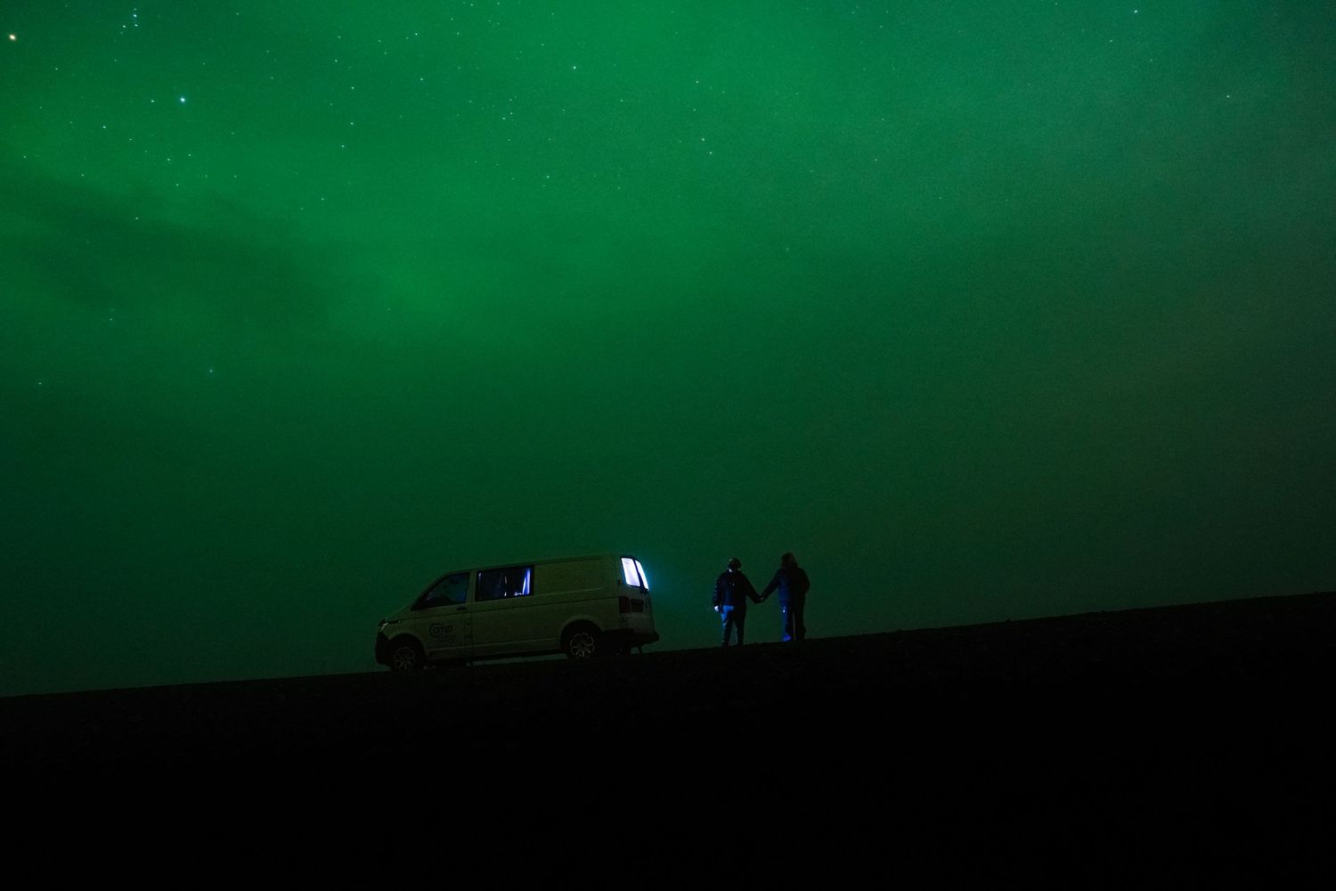 Northern lights dance across a dark green night sky over a silhouetted landscape. Iceland.