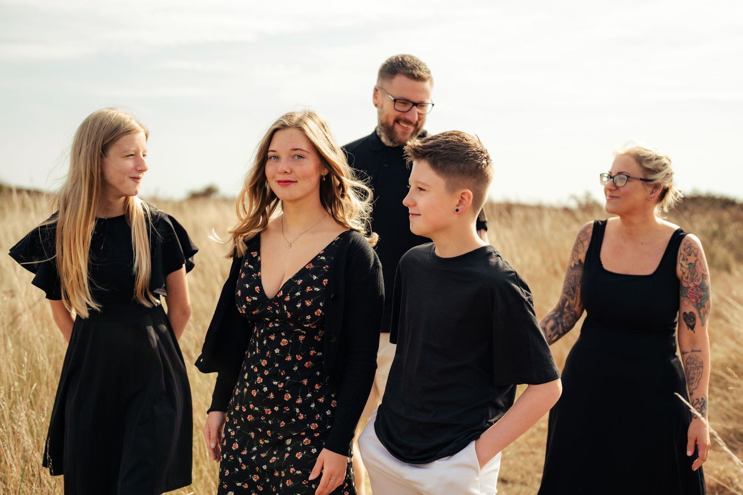 Group of friends laughing and walking together in casual black outfits outdoors. Earlhams Beach, Harwich, Essex.