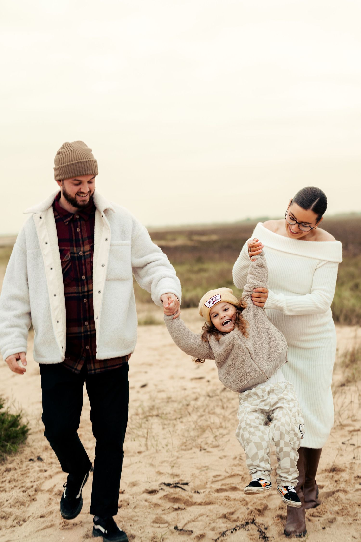 Family enjoying playful moments together on a beach in winter clothing. Earlhams Beach, Harwich, Essex.