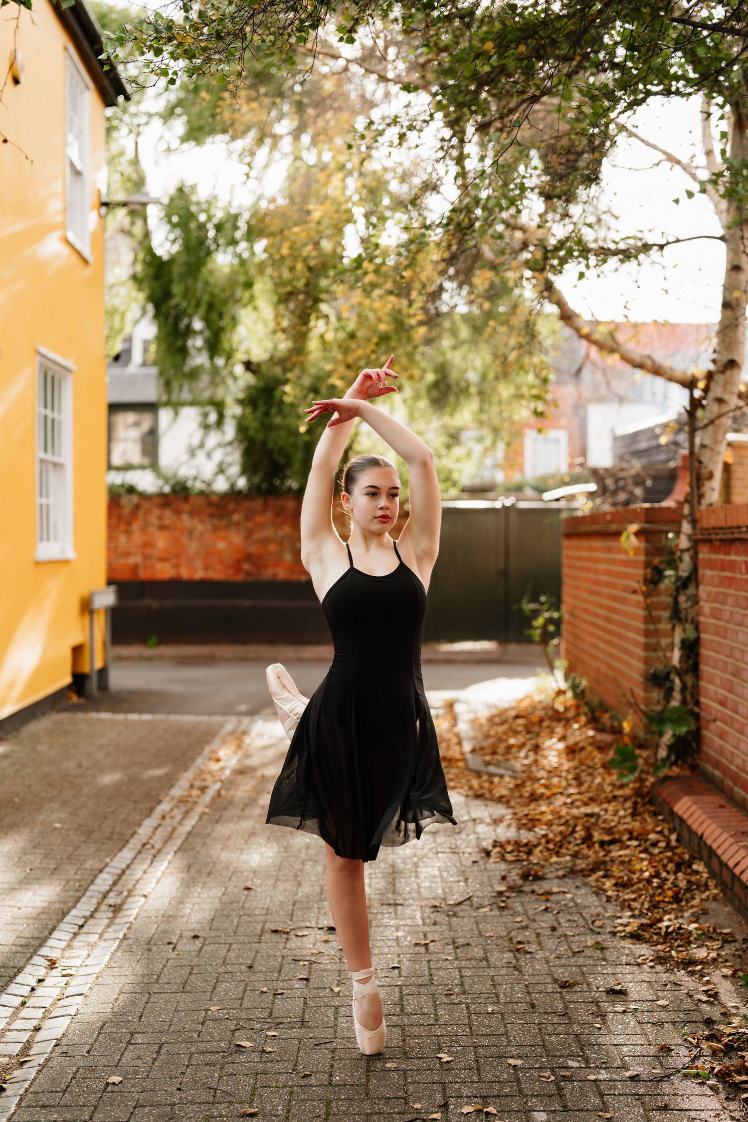 Ballet dancer practicing elegant movements outdoors on a brick-lined path with autumn leaves. Old Harwich, Essex.