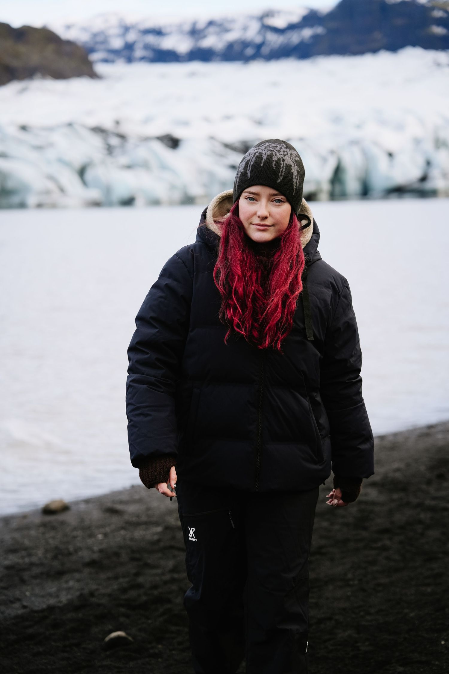 A person in winter clothing stands against a backdrop of snowy glaciers in Iceland.