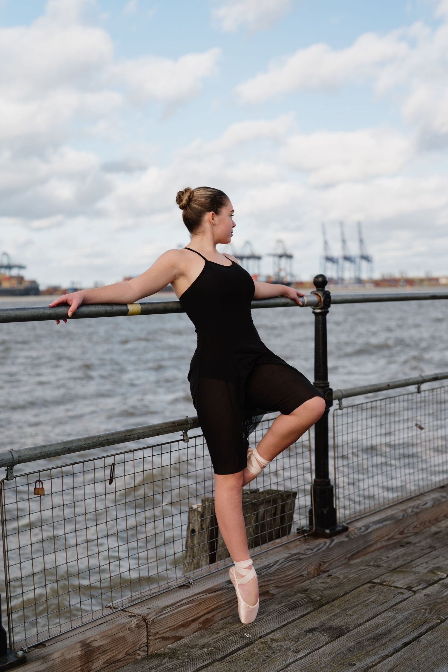 Dancer in black leotard stretches on wooden pier with harbour view. Old Harwich, Essex.