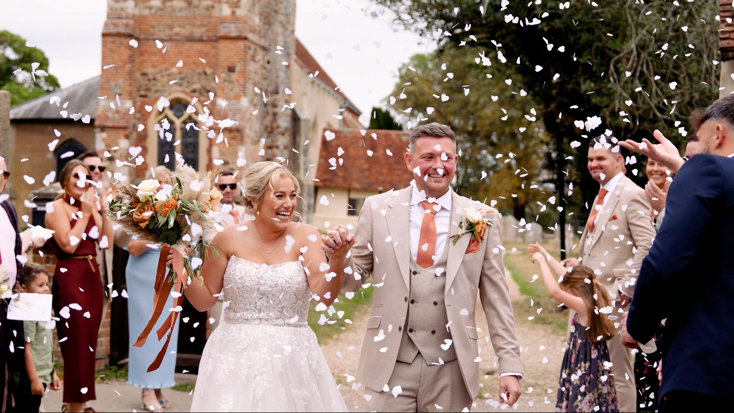 Wedding guests throwing confetti outside a historic stone church. Suffolk.