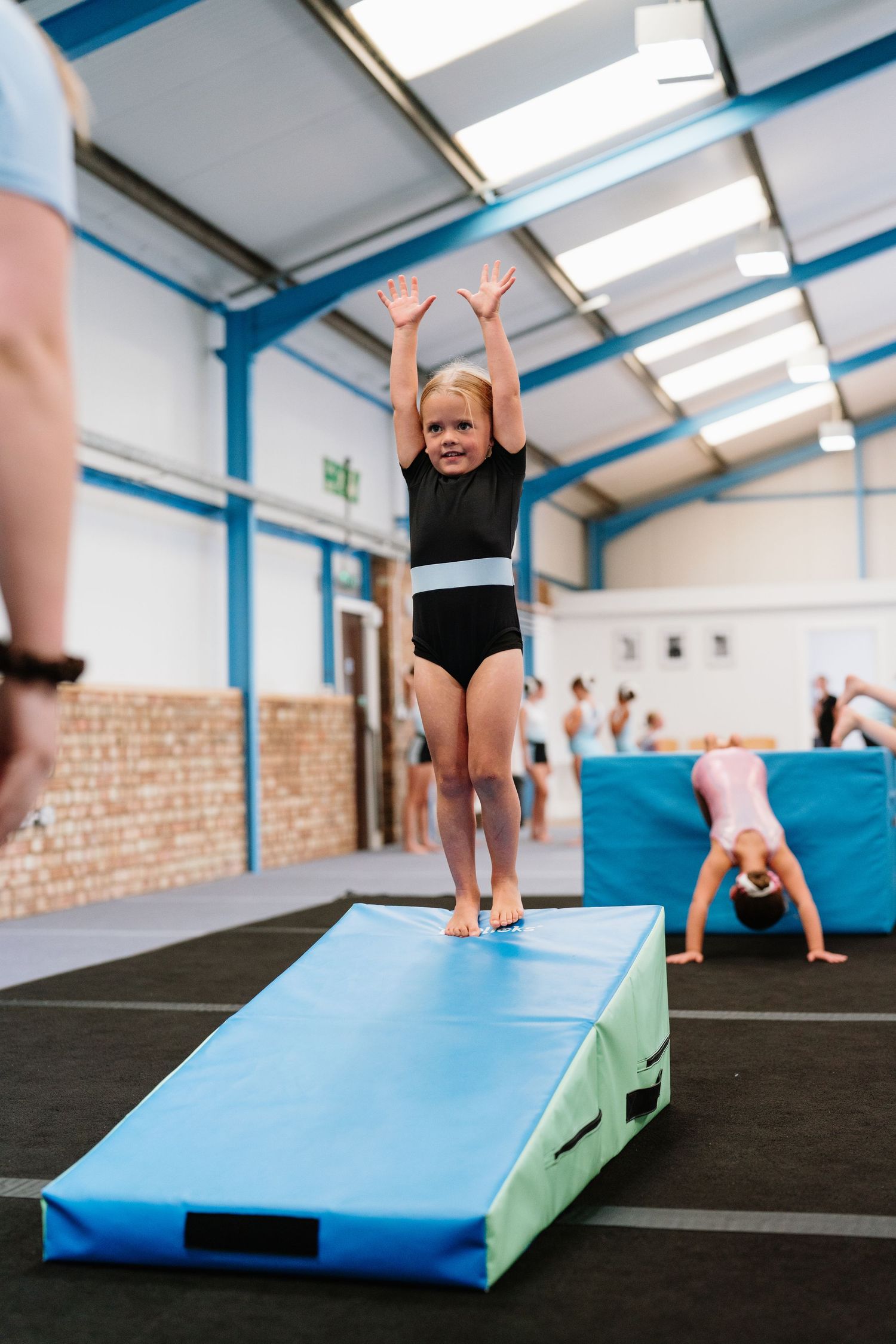 Young gymnast practicing handstands and tumbling skills on blue training mats in a bright gymnasium. Manningtree, Essex.