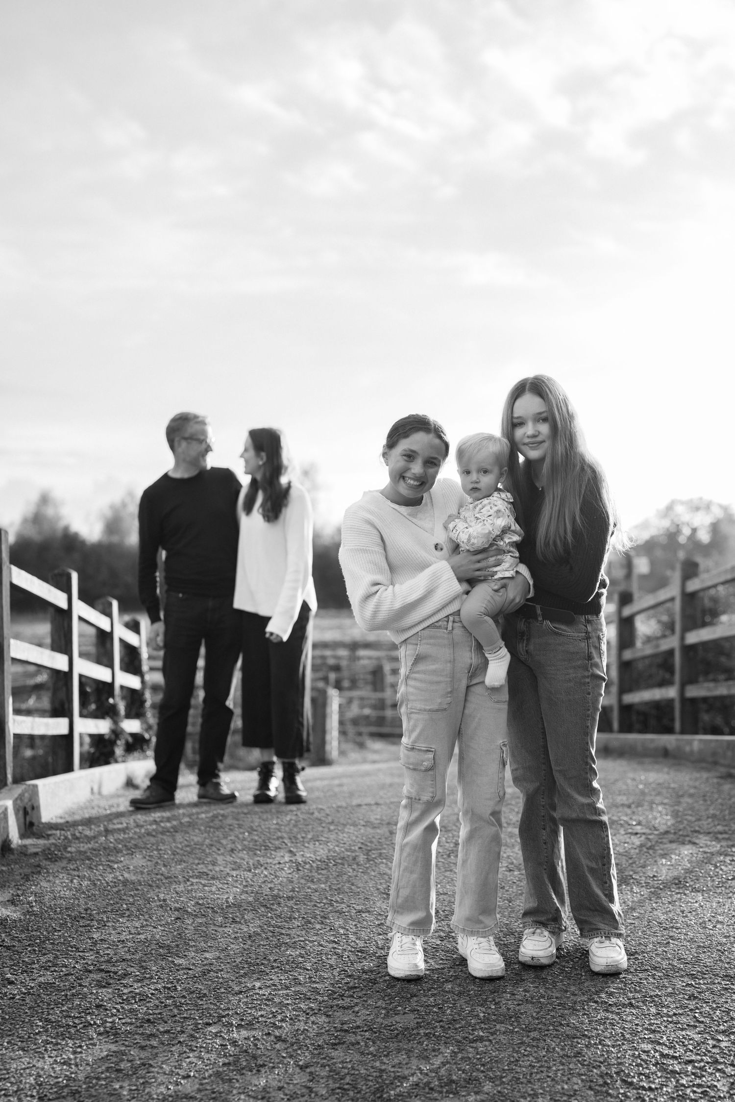 Family members walk together on a path with white fencing during a black and white photoshoot. Flatford Mill.