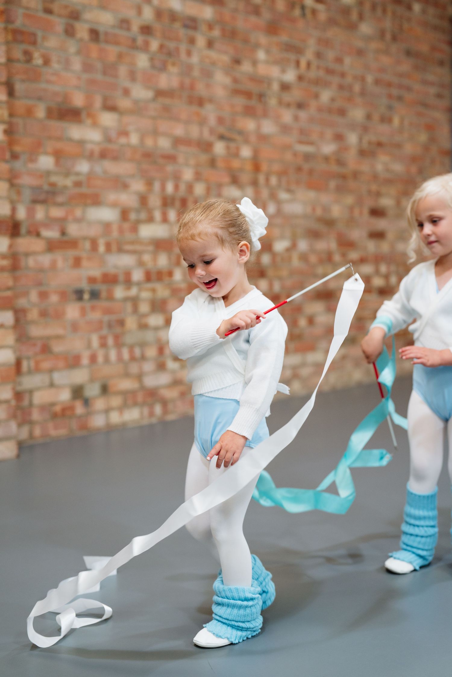 Young dancers in white and blue outfits practicing movements against brick wall background. Manningtree, Essex.