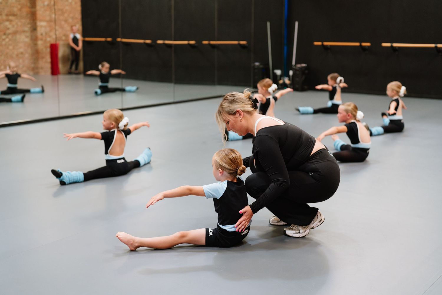 Dance instructor assists student with stretching technique while others practice in a studio class. Manningtree, Essex.