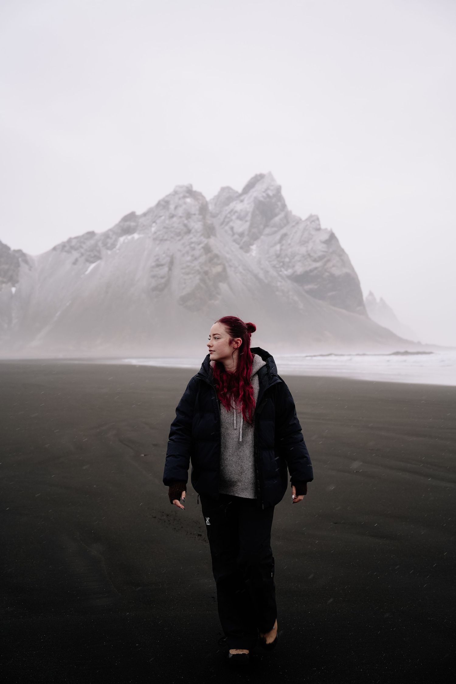 Snow-capped mountains rise behind a dark volcanic beach in Iceland.