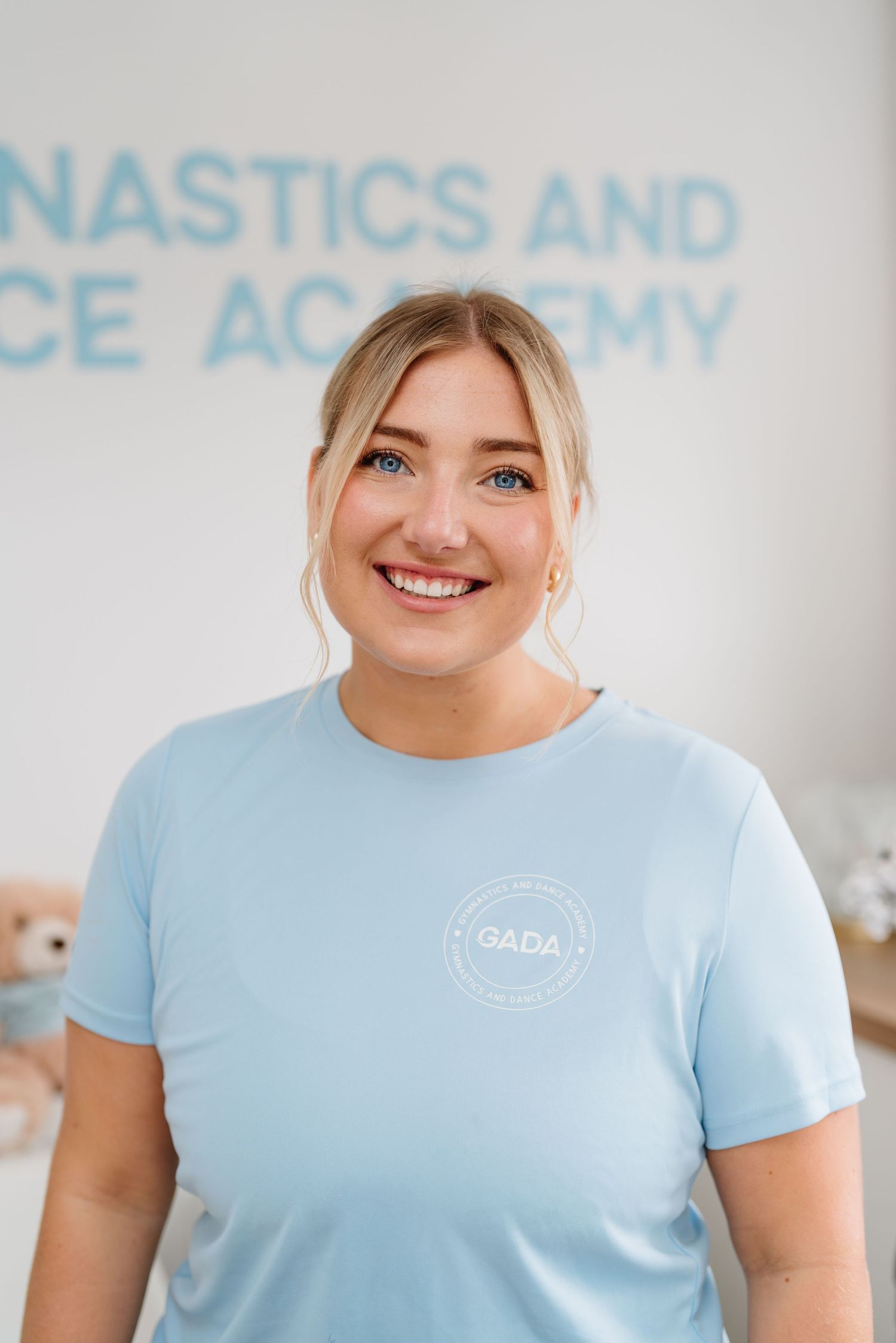 Staff member in light blue uniform shirt smiling at gymnastics academy. Manningtree, Essex.