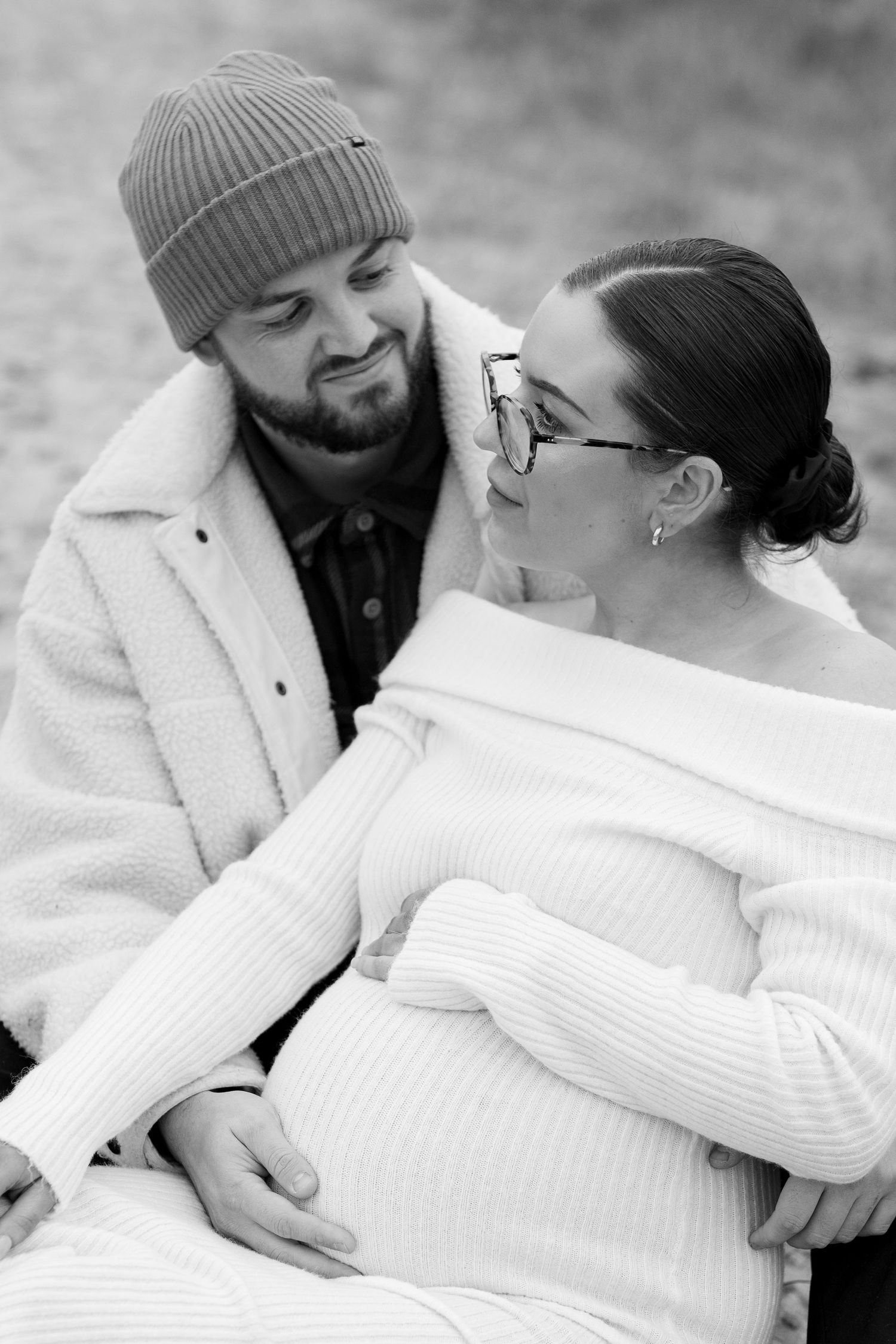 A couple in winter attire share an intimate moment in black and white photography. Earlhams Beach, Harwich, Essex.