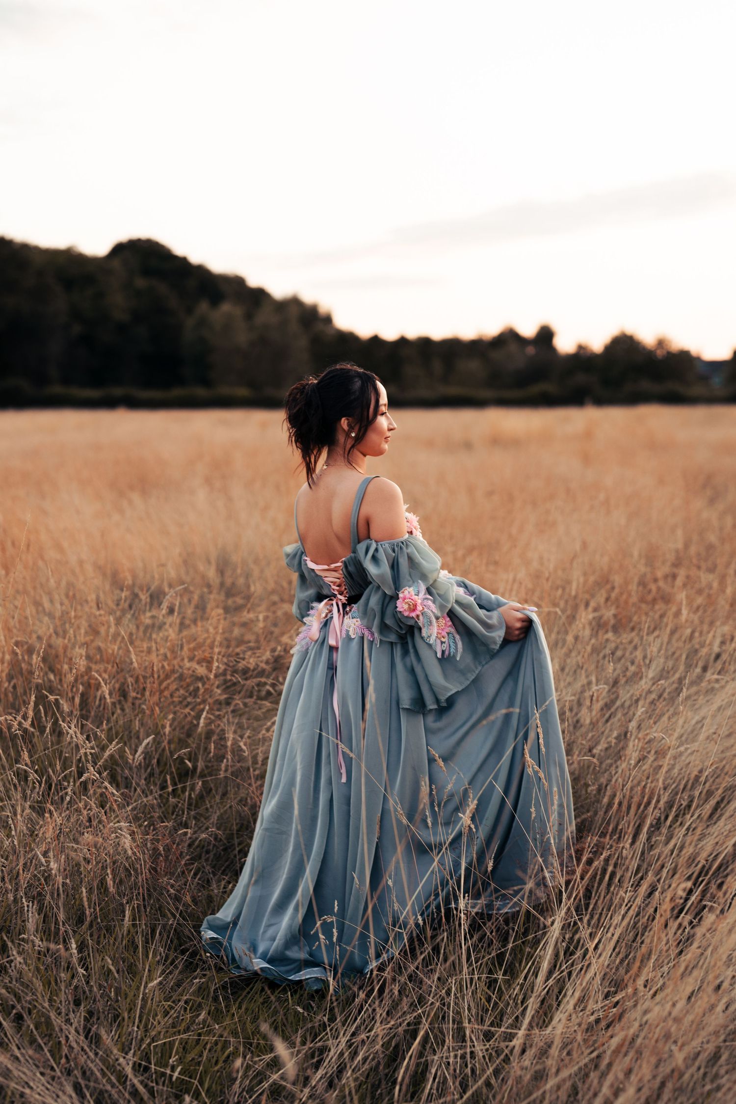 Romantic photoshoot in a golden field featuring a flowing dusty blue dress with delicate pink embellishments. Wrabness, Essex.